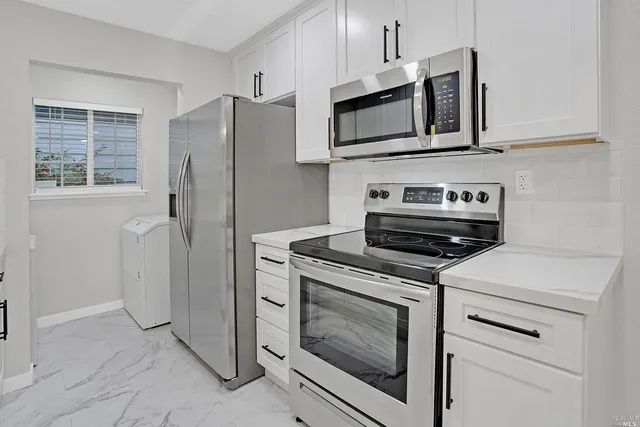 a kitchen with stainless steel appliances granite countertop white cabinets a refrigerator a stove and a sink