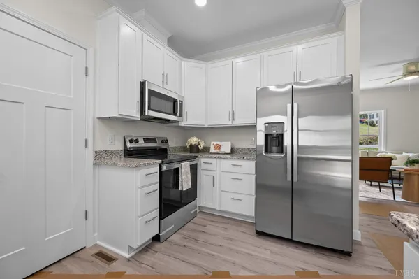 a kitchen with stainless steel appliances granite countertop a refrigerator a stove a sink and white cabinets with wooden floor