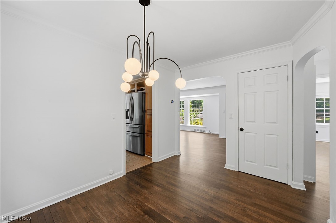 7750 Lewis Road Olmsted Falls, OH 44138 - Photo 12 of 50 Modern chandelier with frosted globe lights, dark wood-finish flooring, white paneled door, arched doorways, and white baseboards