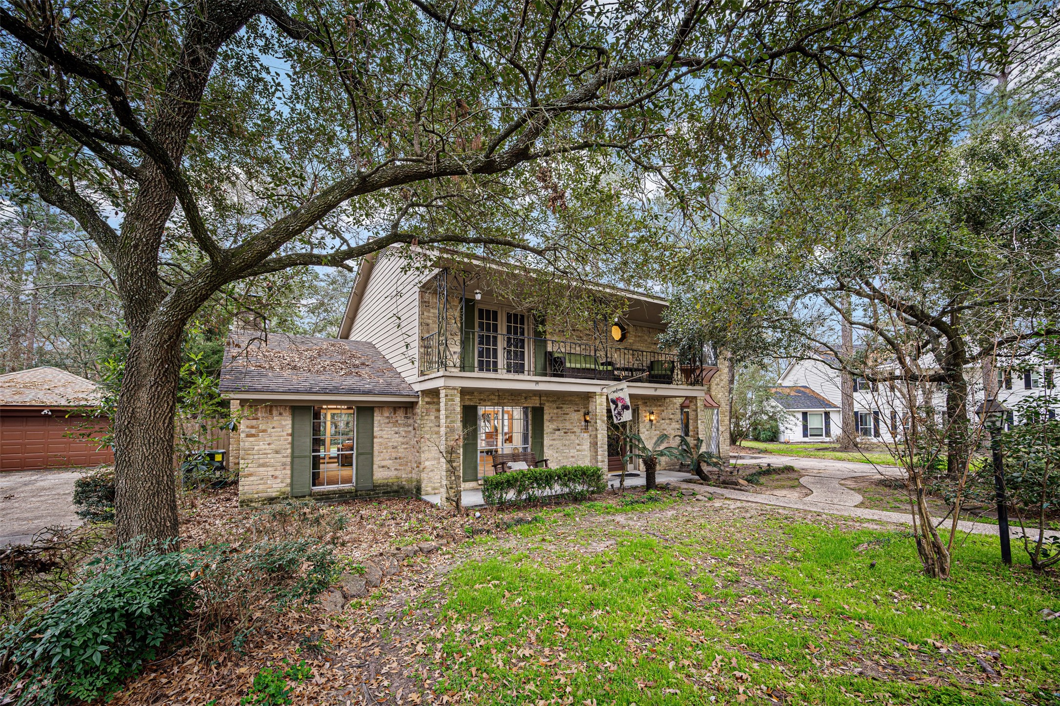 6511 Elmgrove Road Spring, TX 77389 - Photo 4 of 33 Charming two-story brick house surrounded by mature trees, featuring a spacious front lawn and a welcoming balcony. The home has large windows and a charming, inviting atmosphere.