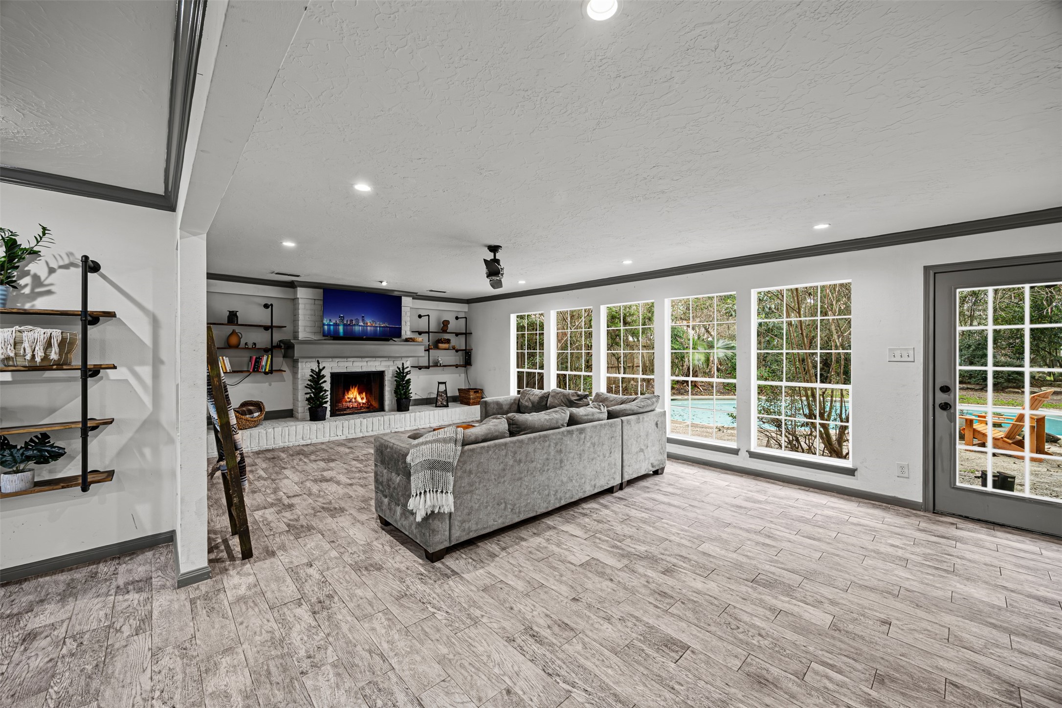 6511 Elmgrove Road Spring, TX 77389 - Photo 6 of 33 This spacious living room features large windows overlooking a pool, a cozy fireplace, modern built-in shelves, and sleek, modern tile flooring, creating an inviting and bright atmosphere.