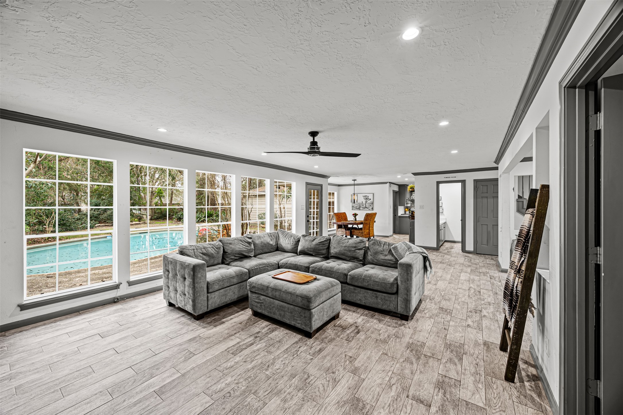 6511 Elmgrove Road Spring, TX 77389 - Photo 9 of 33 This spacious living area features large windows overlooking a pool, offering plenty of natural light. The room has modern tile flooring and flows seamlessly into a dining space and kitchen, creating an ideal open-concept layout and perfect flow between rooms.