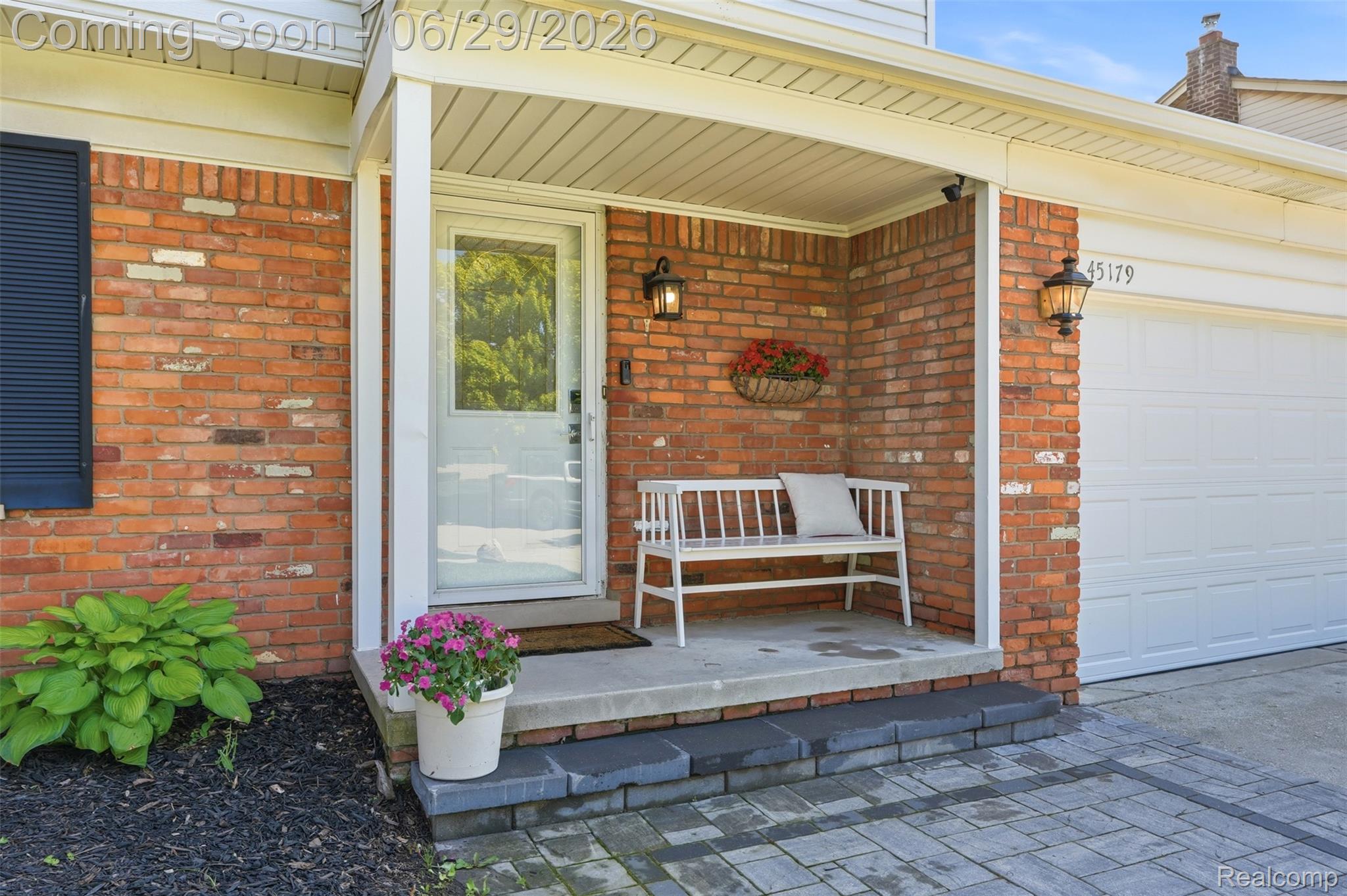 45179 Rudgate Road Canton, MI 48188 - Photo 3 of 48 Brick exterior featuring a covered porch entry, white paneled garage door, black louvered shutters, and decorative outdoor lighting fixtures