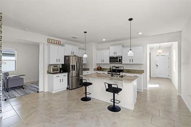 a kitchen with stainless steel appliances kitchen island granite countertop a refrigerator a stove a sink a oven and a dining table with wooden floor