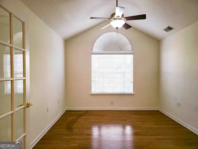 an empty room with wooden floor chandelier fan and windows
