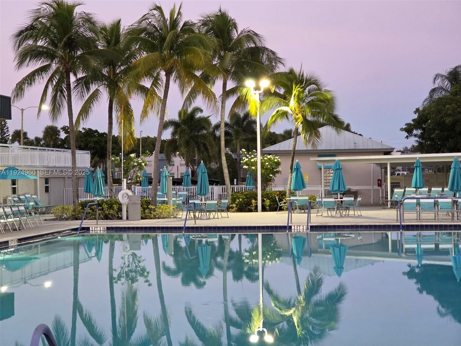 612 Normandy Lane, Unit 612 Delray Beach, FL 33484 - Photo 16 of 18 a patio with water view fountain with table and chairs under an umbrella with palm trees
