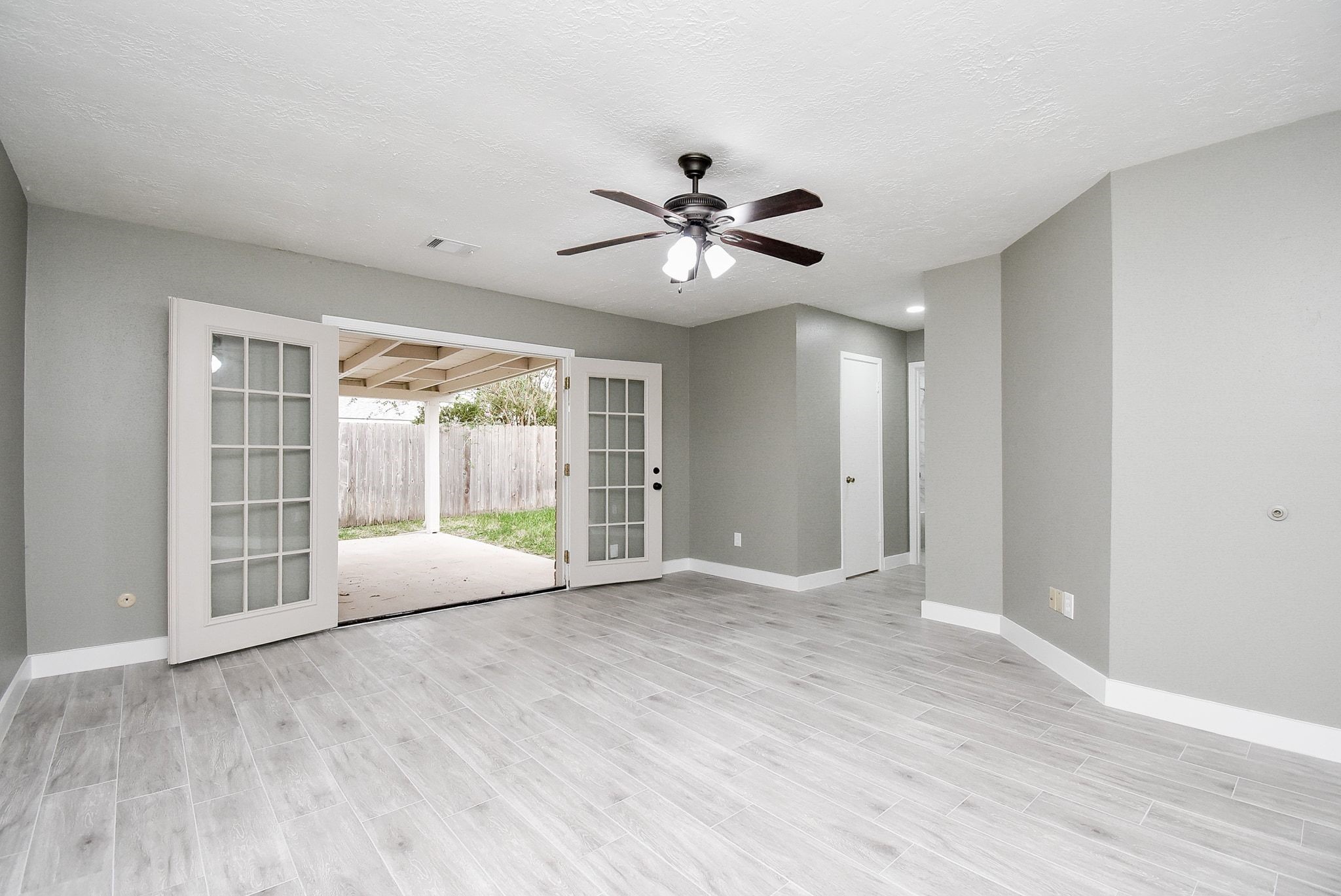 17330 Modbury Drive Spring, TX 77379 - Photo 20 of 30 Spacious Primary bedroom with sleek gray flooring, ceiling fan, and elegant French doors leading to a covered patio and fenced backyard.