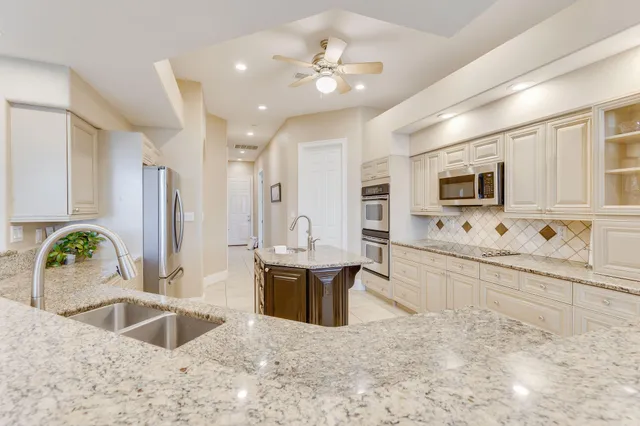 a large white kitchen with kitchen island a sink a counter top space and stainless steel appliances