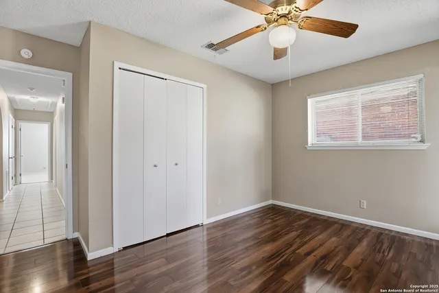 an empty room with wooden floor chandelier fan and windows