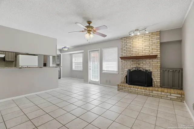 a living room with a fireplace furniture a ceiling fan and a window
