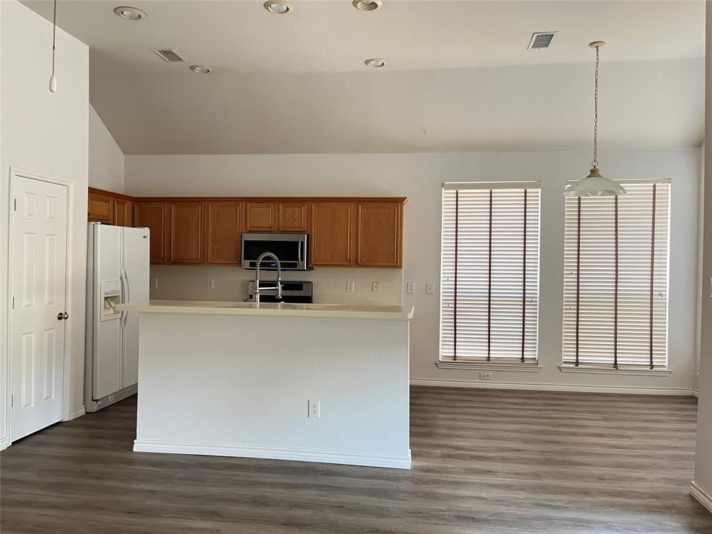 9814 Glenshee Drive Rowlett, TX 75089 - Photo 7 of 25 Kitchen featuring hanging light fixtures, stainless steel appliances, lofted ceiling, dark wood-style floors, and brown cabinetry
