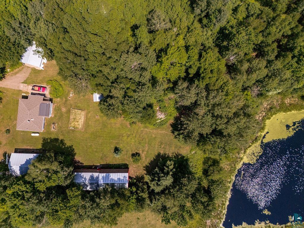 2592 Strandberg Road Barnum, MN 55707 - Photo 6 of 44 Aerial view of a property featuring a brown-roofed residence with solar panels, a secondary building with a light-colored roof, a third elongated structure with a light-colored roof, and a visible pond