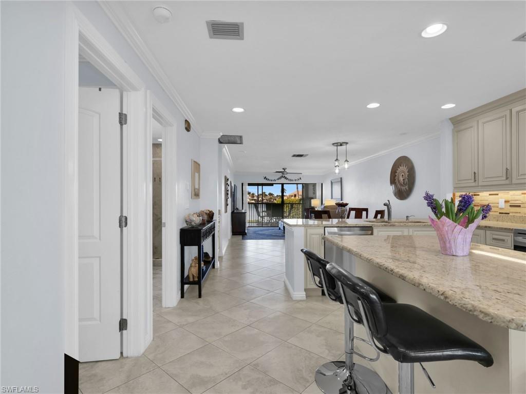 750 West Elkcam Circle, Unit 107 Marco Island, FL 34145 - Photo 32 of 33 Kitchen featuring crown molding, a breakfast bar area, pendant lighting, open floor plan, and light stone counters