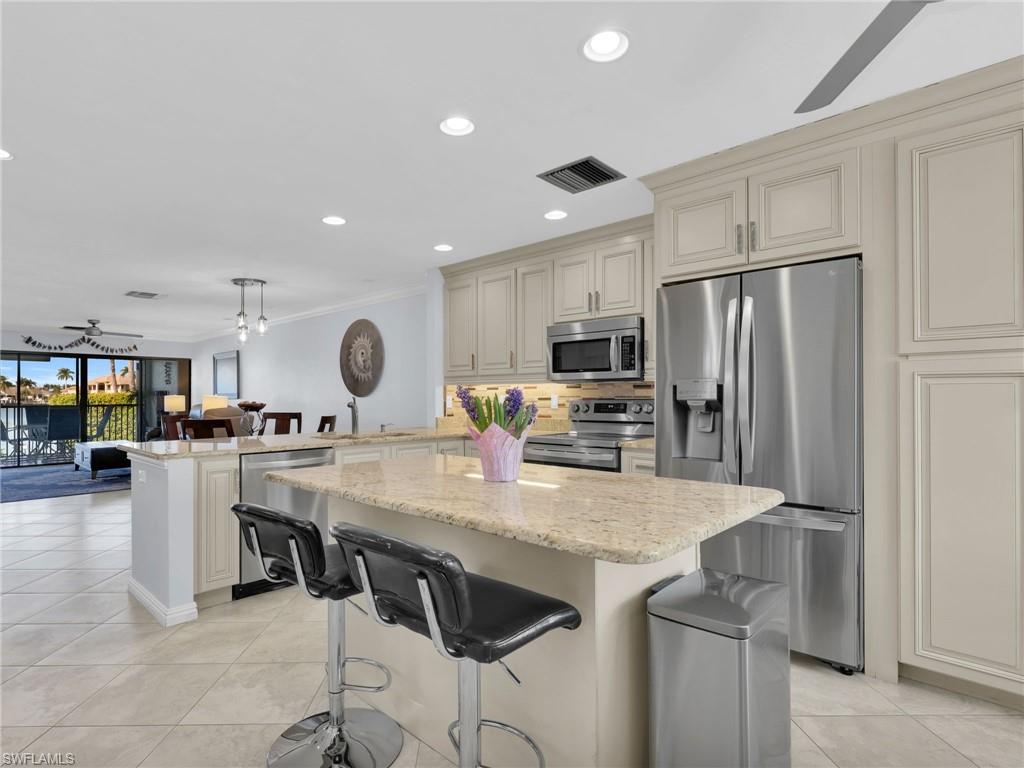 750 West Elkcam Circle, Unit 107 Marco Island, FL 34145 - Photo 4 of 33 Kitchen featuring ceiling fan, a breakfast bar area, appliances with stainless steel finishes, light stone countertops, and ornamental molding