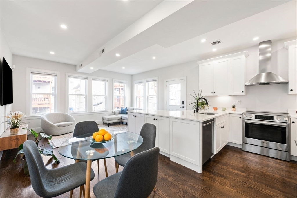 12-14 Porter Street, Unit 12 Boston, MA 02130 - Photo 5 of 37 a large white kitchen with stainless steel appliances granite countertop a stove a sink a dining table and chairs