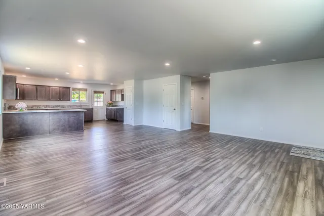an empty room with wooden floor and kitchen view