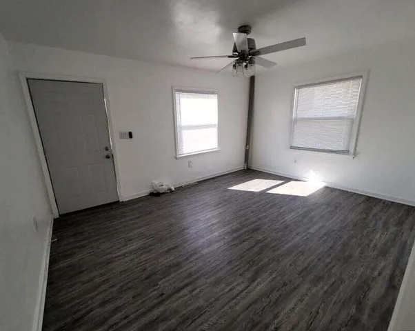 an empty room with wooden floor fan and windows