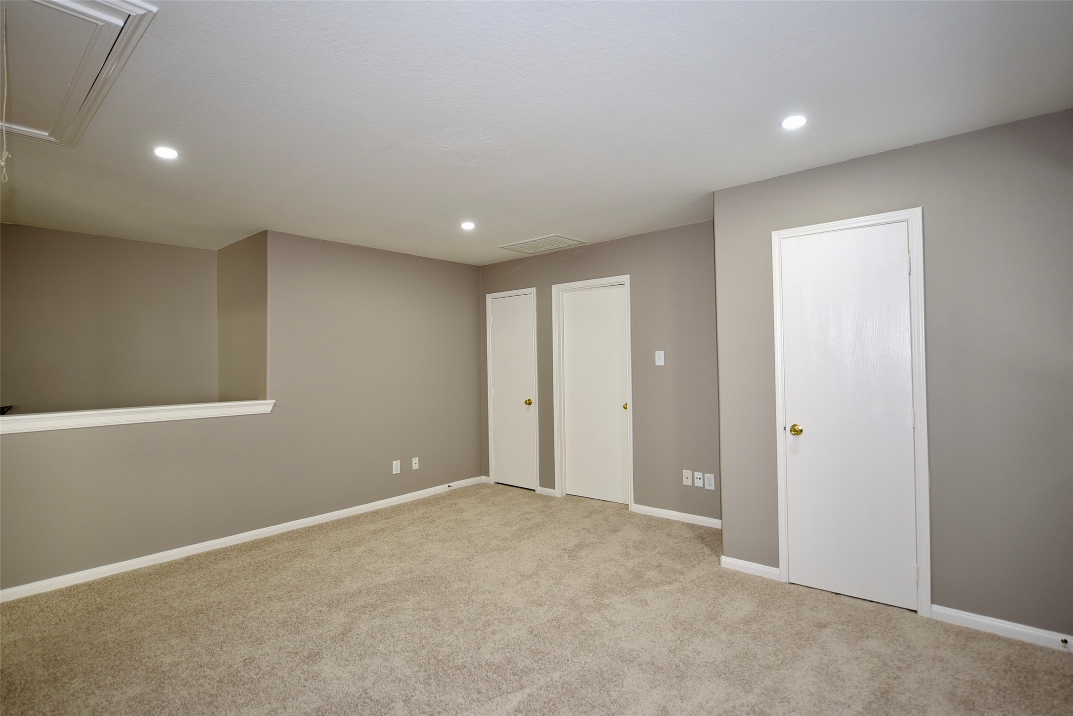 9611 Babbling Spring Court Tomball, TX 77375 - Photo 18 of 31 This photo shows a spacious, carpeted room with neutral-colored walls, recessed lighting, and two white doors. It's ideal for a versatile living space or home office.