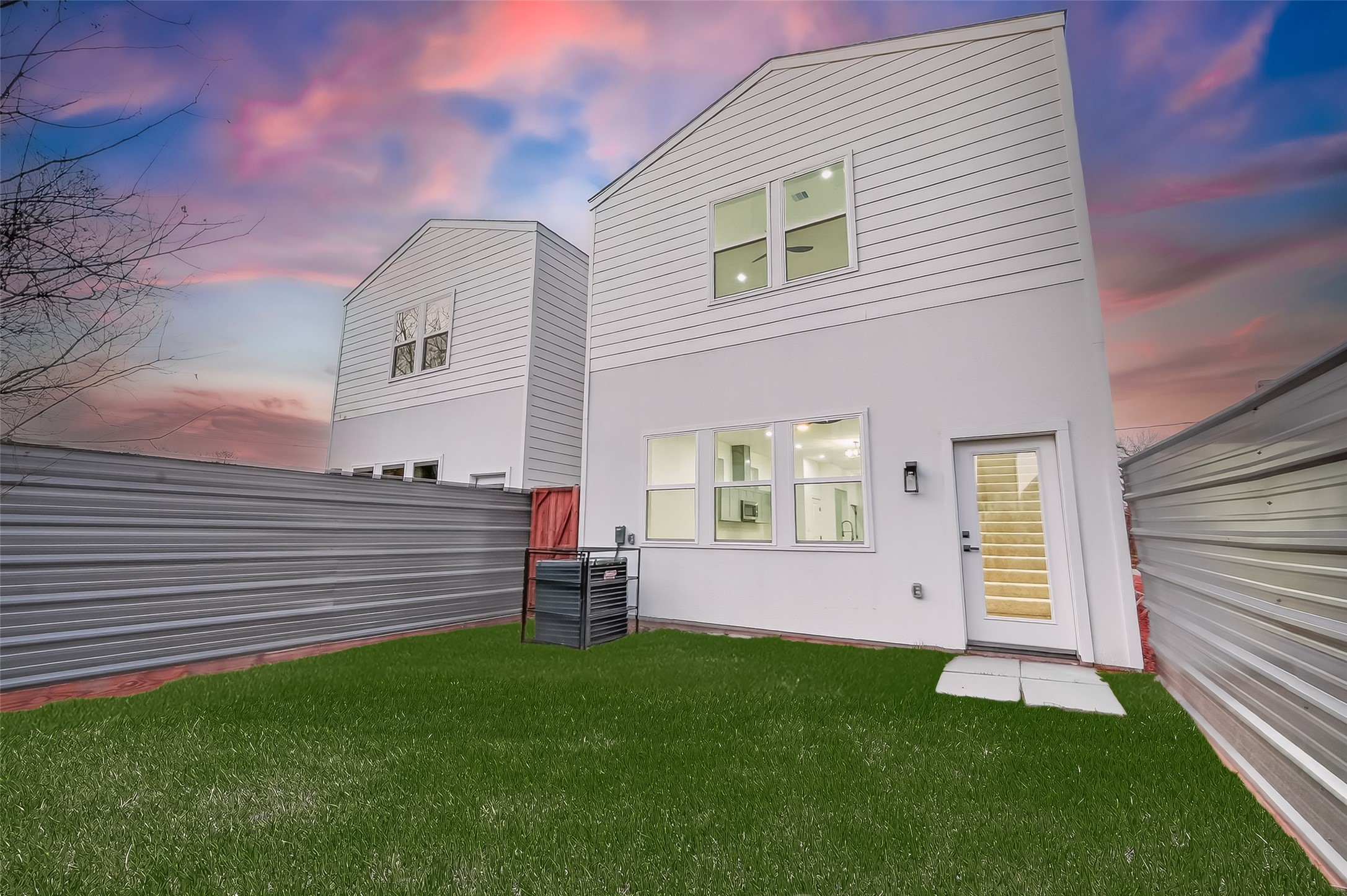 3514 Good Hope Street, Unit B Houston, TX 77021 - Photo 25 of 26 Modern two-story home with a clean white exterior, fenced yard, and outdoor lighting. Features large windows for ample natural light, complemented by a well-maintained lawn and a beautiful sunset backdrop.