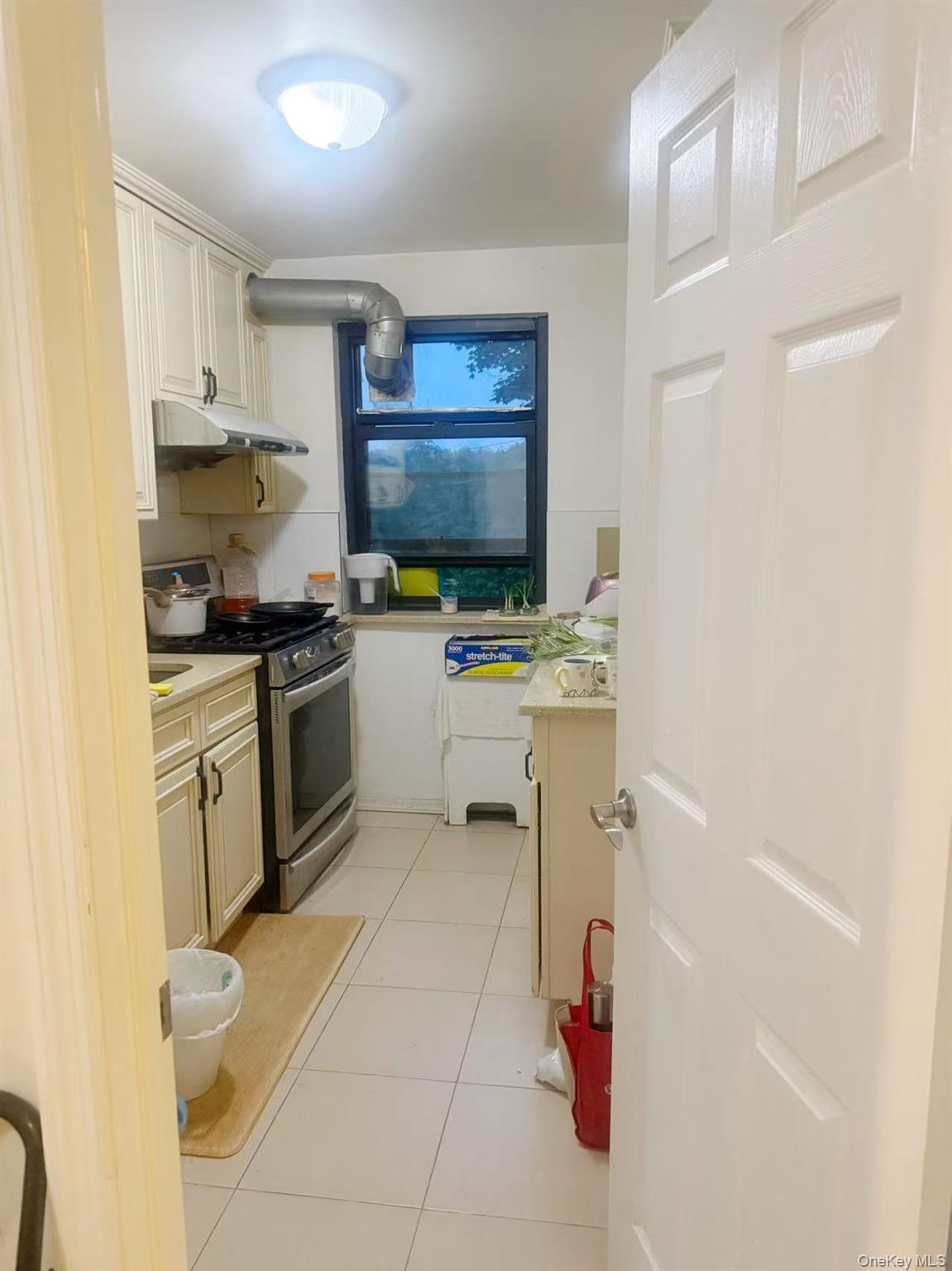 46 Terrace Circle, Unit 2C Great Neck, NY 11021 - Photo 11 of 14 Kitchen featuring stainless steel range with gas stovetop, under cabinet range hood, light tile patterned floors, light countertops, and cream cabinetry