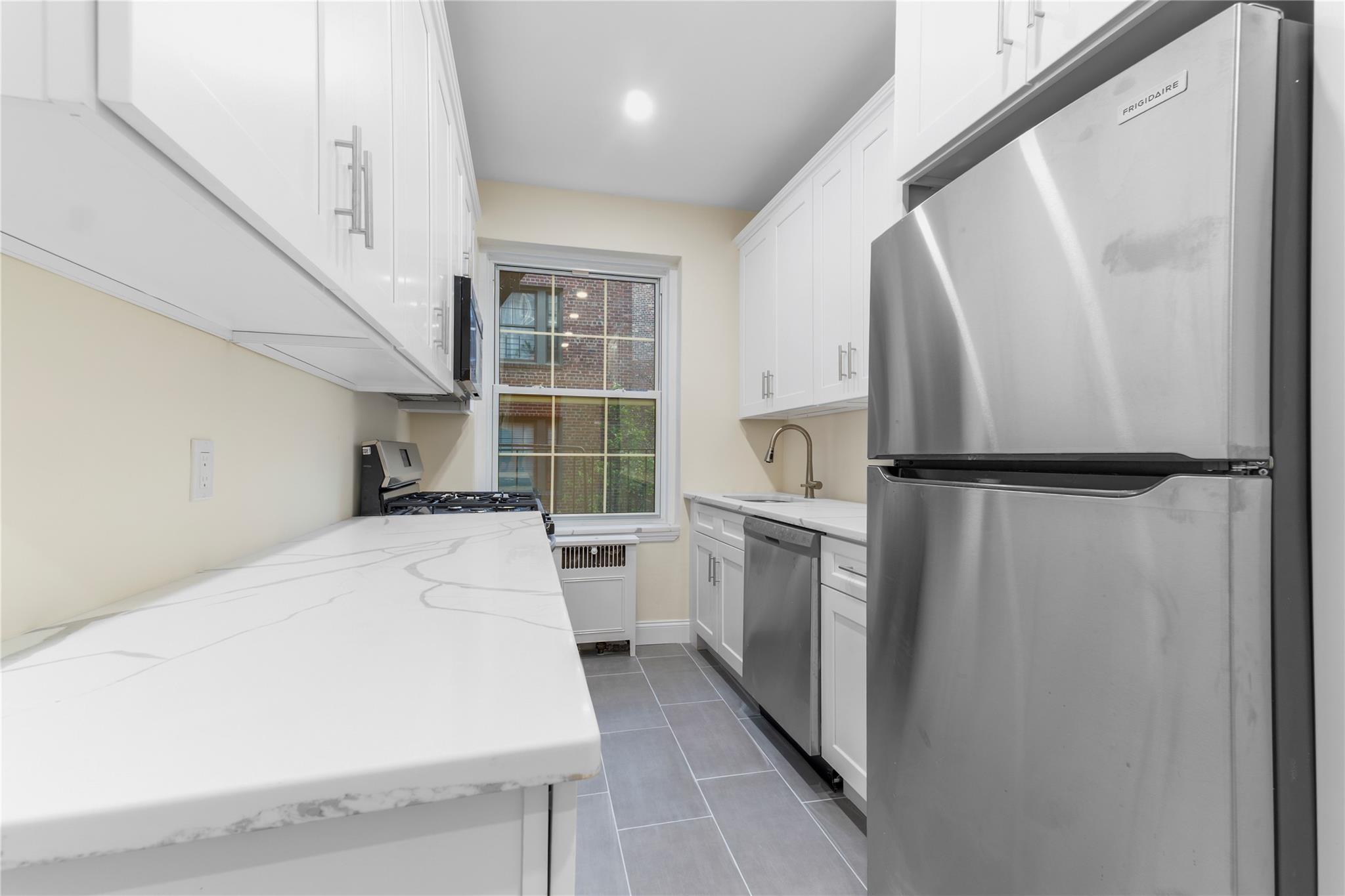 110-07 73rd Road, Unit 4D Queens, NY 11375 - Photo 10 of 16 Kitchen with appliances with stainless steel finishes, white cabinets, dark tile patterned flooring, light stone counters, and a sink