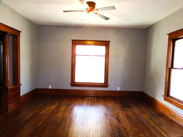 an empty room with wooden floor chandelier fan and windows