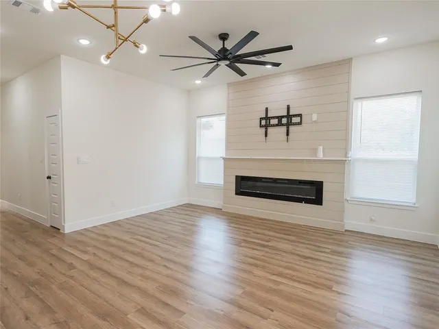 an empty room with wooden floor a ceiling fan a fireplace and windows