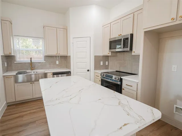 a kitchen with stainless steel appliances a stove top oven a sink a refrigerator white cabinets and wooden floor