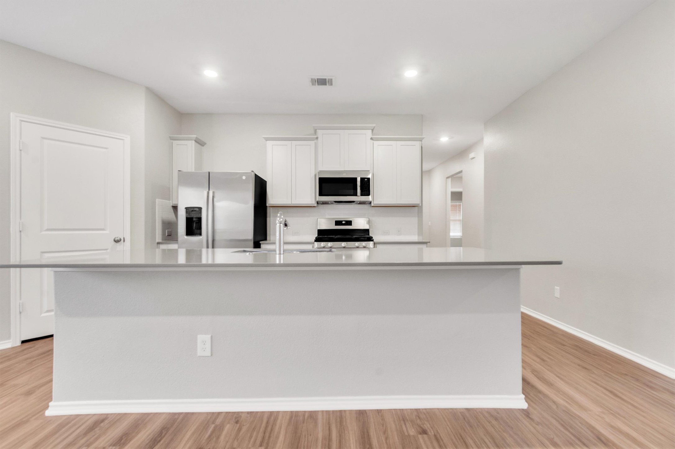 301 Blue Springs Pass Kyle, TX 78640 - Photo 14 of 20 Kitchen featuring white cabinetry, stainless steel fridge, a center island with sink, gas stove, and light wood-type flooring