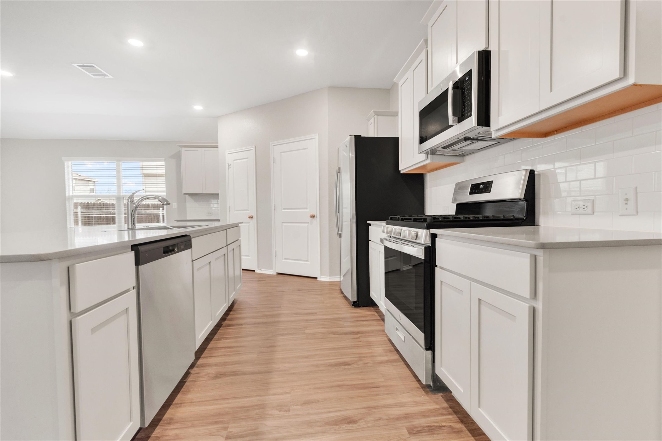 301 Blue Springs Pass Kyle, TX 78640 - Photo 16 of 20 Kitchen featuring stainless steel appliances, white cabinets, light wood-style floors, a kitchen island with sink, and recessed lighting