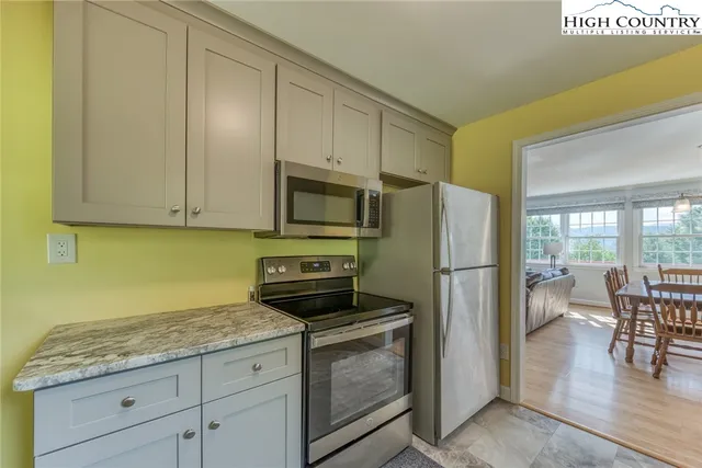 a kitchen with granite countertop a refrigerator a stove a sink and white cabinets with wooden floor