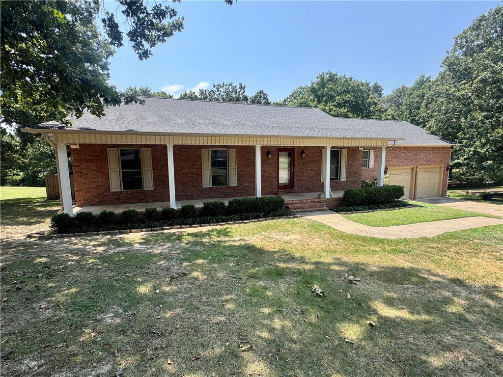 Brick ranch-style residence featuring a welcoming covered porch with white columns, a red front door, and a two-car garage