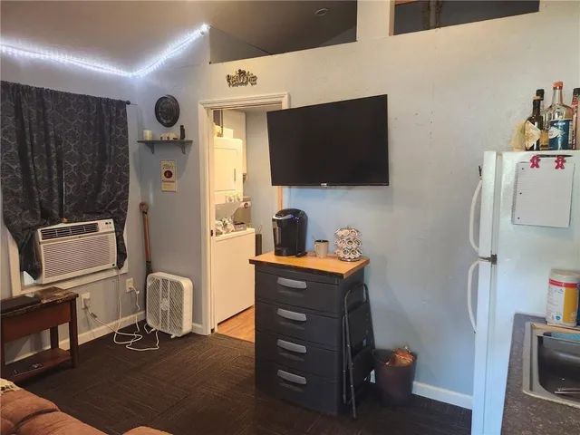 a room with a flat screen tv dressers and a refrigerator