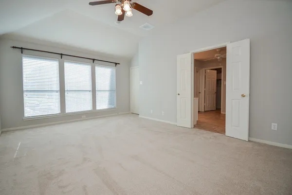 an empty room with a chandelier fan and windows