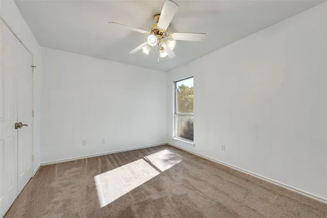 an empty room with chandelier fan and windows