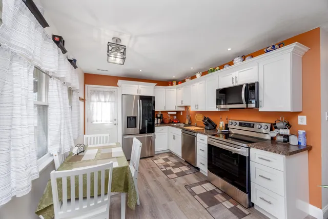 a kitchen with stainless steel appliances granite countertop a stove top oven a sink dishwasher a dining table and chairs with wooden floor