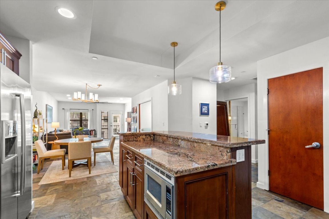 1812 West Avenue, Unit 306 Austin, TX 78701 - Photo 12 of 38 Kitchen featuring hanging light fixtures, stone tile flooring, appliances with stainless steel finishes, and dark stone counters
