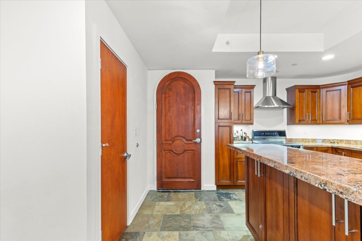 1812 West Avenue, Unit 306 Austin, TX 78701 - Photo 16 of 38 Kitchen featuring brown cabinetry, range with electric cooktop, stone finish floor, baseboards, and wall chimney exhaust hood