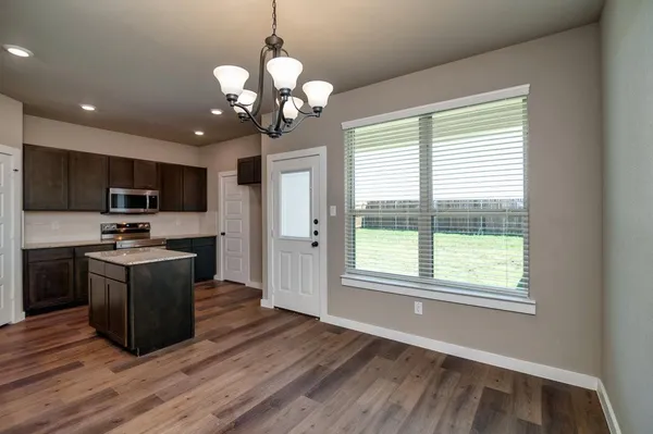 a kitchen with stainless steel appliances granite countertop a refrigerator a sink dishwasher a oven and a dining table with wooden floor
