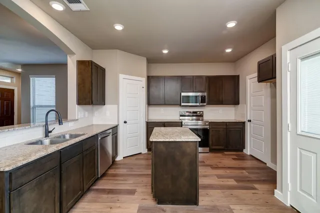 a large kitchen with stainless steel appliances kitchen island granite countertop a refrigerator and a stove top oven