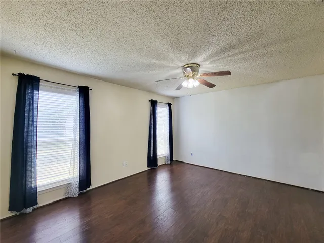 an empty room with wooden floor chandelier fan and windows