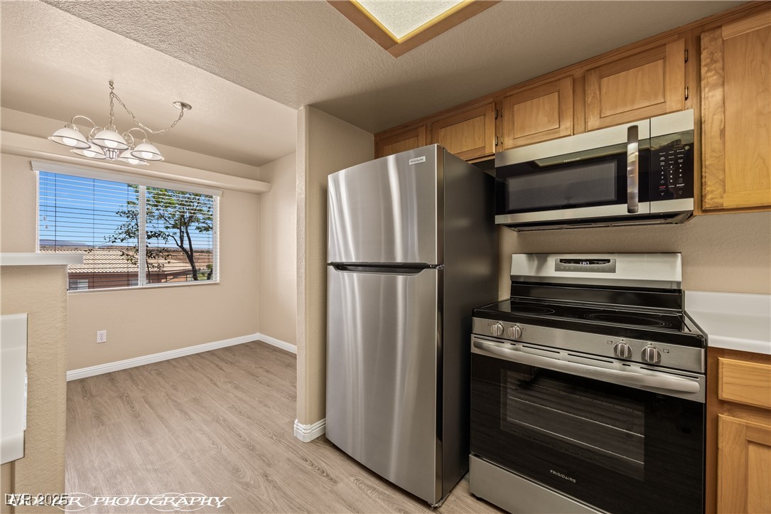 334 Colleen Court, Unit D Mesquite, NV 89027 - Photo 9 of 61 Kitchen with stainless steel appliances, brown cabinets, a chandelier, light countertops, and a textured ceiling