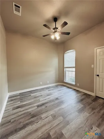 an empty room with wooden floor fan and windows