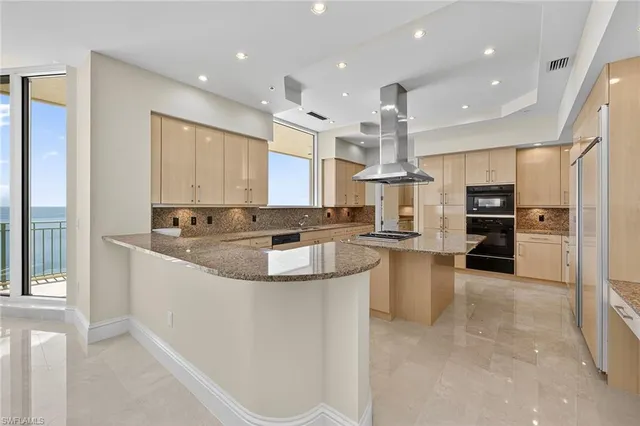 a large kitchen with stainless steel appliances kitchen island granite countertop a large counter top and a view of living room
