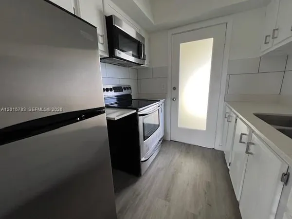 a kitchen with stainless steel appliances a sink a stove top oven a wooden floor and cabinets