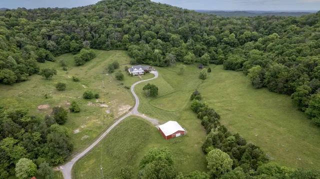 an aerial view of a residential houses with outdoor space and trees all around