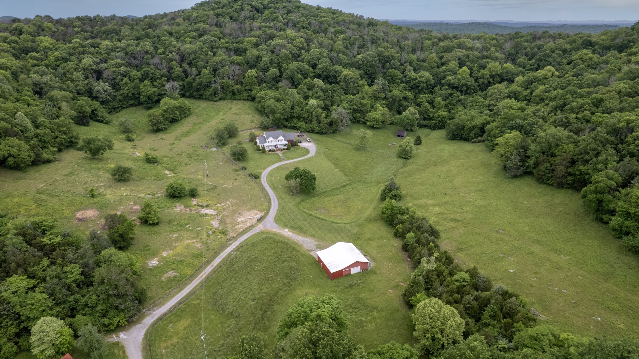 an aerial view of a residential houses with outdoor space and trees all around