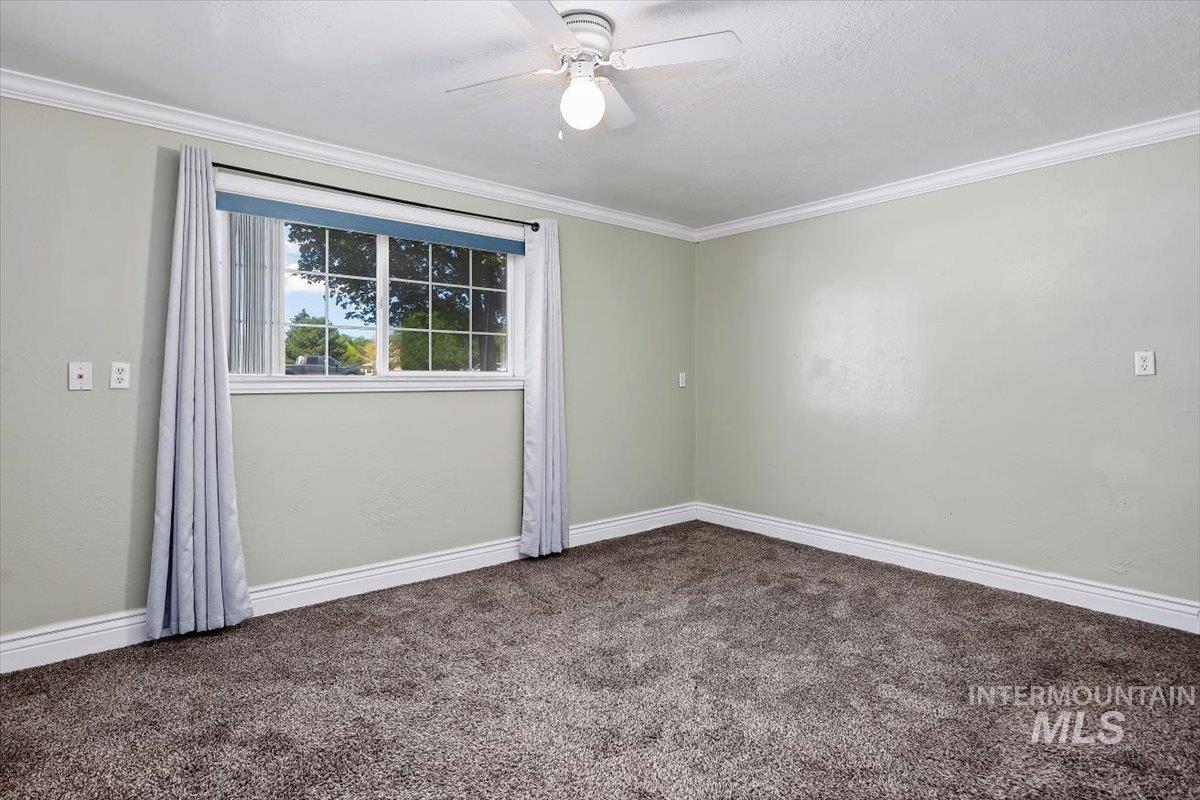 1940 Q Street Heyburn, ID 83336 - Photo 18 of 30 Bright room featuring textured light green walls, a double-paned window with white grilles, white crown molding, and plush gray carpeting