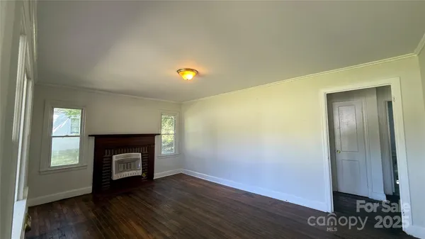 a view of an empty room with wooden floor and a fireplace