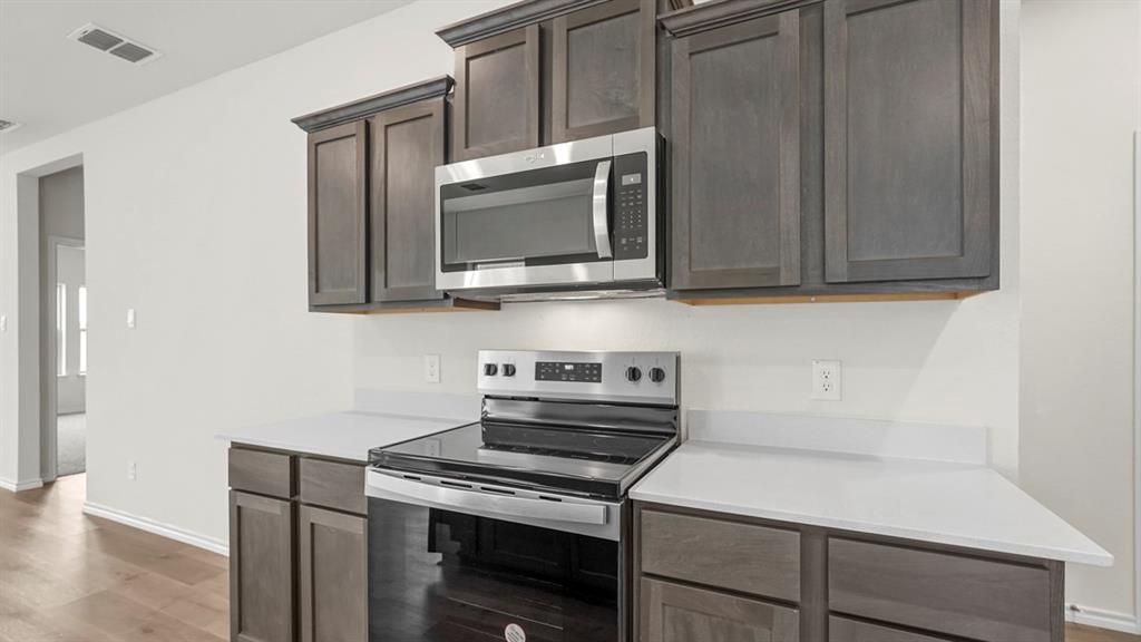 216 Pheasant Run Road Terrell, TX 75160 - Photo 33 of 37 Wood-finish flooring, dark wood-finish cabinetry, white countertops, stainless steel microwave, and stainless steel electric range